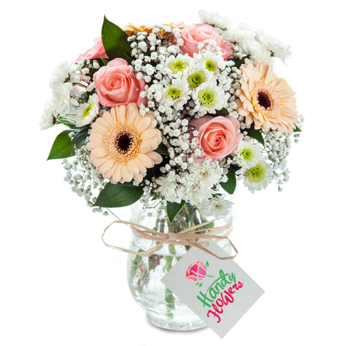 This expertly arranged mixed floral bouquet, inspired by the natural tranquillity of Old Oak Common, showcases a symphony of pastel tones and fresh textures against a spotless white background. Plush peach-pink roses, front and center, offer graceful spiraled blooms that evoke feelings of romance and nostalgia-much like wandering across the nearby Scrubs on a sunny spring day. Flanking the roses, two prominent gerbera daisies in mellow peach shades unfurl their broad petals, drawing the eye with their playful depth and chocolatey centers. Generous sprigs of delicate white gypsophila wind their way through the design, infusing airy fullness and echoing the quiet moments found in local woodland clearings. Crisp white chrysanthemums, their vibrant green cores boldly shining, enhance the bouquet's sense of brightness and renewal, reminiscent of the lively atmosphere at Old Oak Common's farmers markets. Touches of deep green foliage, including eucalyptus, provide grounding accents, introducing subtle fragrance and textural diversity. The stems are artfully gathered within a clear, lightly textured glass vase, water gleaming and stems intertwining in a natural array. A rustic band of twine, knotted simply around the vase's neck, suspends a blank white tag suitable for personalized messages-whether congratulating a new home purchase or sending sympathy to a friend near Old Oak Lane. Bathed in soft, ambient light, this bouquet communicates warmth, sincerity, and the high level of craftsmanship celebrated by florists throughout Old Oak Common.